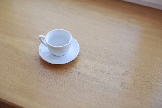 one pure white ceramic Cup and saucer without drink sits on a wooden table in the afternoon sunlight