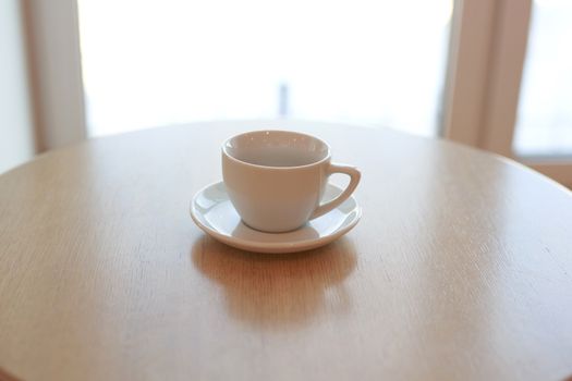 one pure white ceramic Cup and saucer without drink sits on a wooden table in the afternoon sunlight