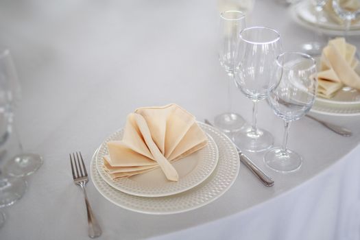 Cutlery on the table, clear glass champagne glasses, white tableware plate with beige peach napkin, knife and fork, table without people, clean tableware without food