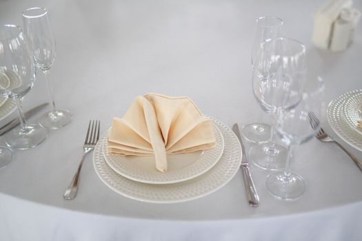 Banquet hall table, white tablecloth, table without food, table setting, glasses empty, waiting room Banquet without people, appliances on the table knife and fork, beige napkin