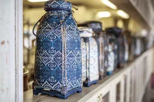 vase in Oriental style with intricate ornament stands on a light wooden vintage shelf, in a row of many vintage vases, blurred background