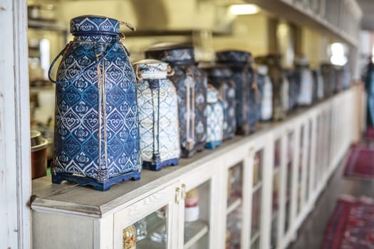 vase in Oriental style with intricate ornament stands on a light wooden vintage shelf, in a row of many vintage vases, blurred background