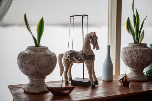 decorative wooden horse stands on the table near the window flowers in pots, white bottle, iron boat, elements of room decoration, decor, Provence, delicate tones