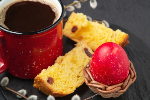 Red Easter egg, a slice of Easter cake and a cup of coffee on a cutting board on a dark table - traditional Easter breakfast