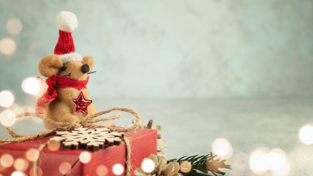 Little toy Christmas mouse, gift and decorations on a gray table. Christmas composition with the symbol of 2020 according to the Chinese horoscope, horizontal banner with copy space.