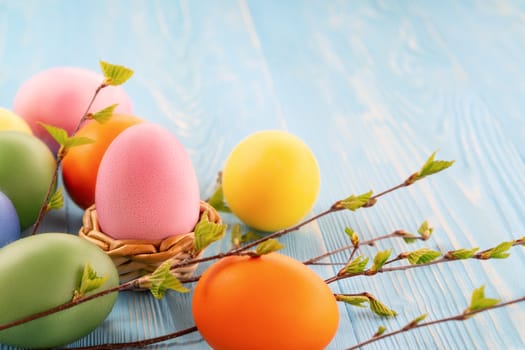 Multi-colored Easter eggs on a blue wooden table with twigs of birch with young leaves - Easter composition with copy space.