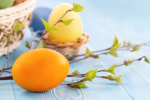 Multi-colored Easter eggs on a blue wooden table with twigs of birch with young leaves - Easter composition with copy space.