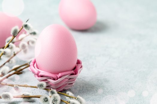 Pink Easter eggs in a wicker stand and on a gray table with pussy-willow twigs - Easter composition with copy space.