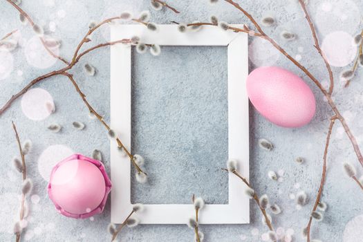 Pink easter eggs on gray table with willow twigs and white wooden frame - easter composition with copy space, flatlay,