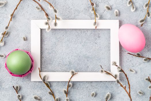 Pink and green easter eggs on gray table with willow twigs and white wooden frame - easter composition with copy space, flatlay,