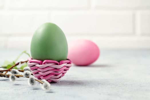 Pink and green Easter eggs in a wicker stand and on a gray table with pussy-willow twigs - Easter composition with copy space.