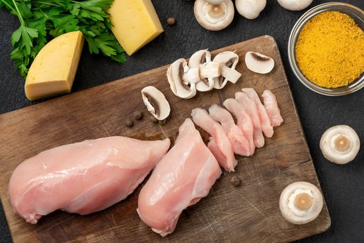 Slicing chicken breast fillet for cooking with champignons and cheese, top view.