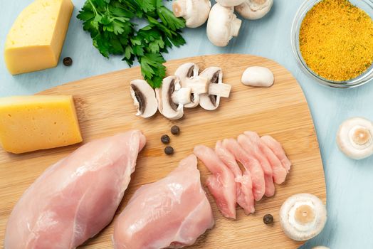 Slicing chicken breast fillet for cooking with champignons and cheese, top view.