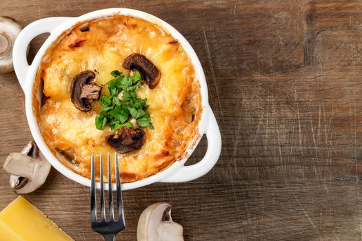 Casserole with chicken, mushrooms and cheese known in Russia as julienne in white bowl with herbs on a wooden board, top view, flat lay, copy space.