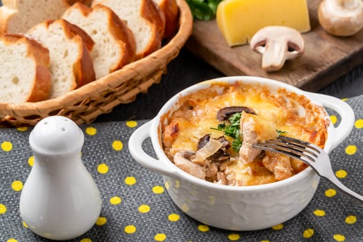 Casserole with chicken, mushrooms and cheese, known in Russia as julienne in white bowl with herbs on a kitchen towel.