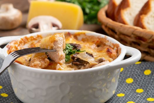 Casserole with chicken, mushrooms and cheese, known in Russia as julienne in white bowl with herbs on a kitchen towel, close up.