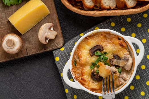 Casserole with chicken, mushrooms and cheese, known in Russia as julienne in white bowl with herbs on a kitchen towel, top view, flat lay.