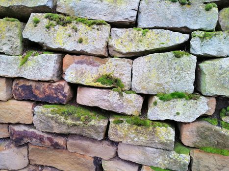 Old stone wall with moss and holes texture background.