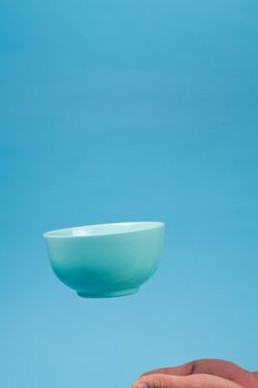 A blue ceramic mattle deep bowl for breakfast flying under male hands on blue background. Ideal photo for levitation of food and fruits or nuts.