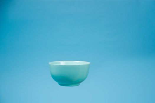 A blue ceramic mattle deep bowl for breakfast flying on blue background. Ideal photo for levitation of food and fruits or nuts.