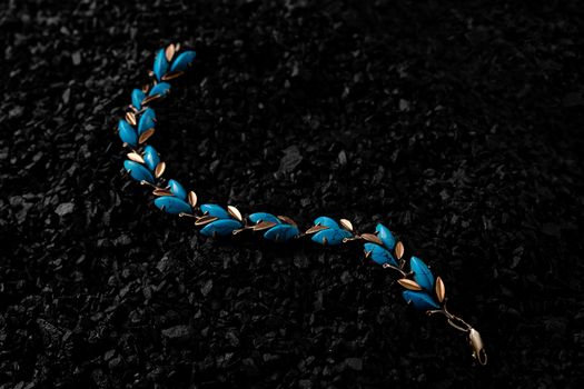 Unique handmade golden bracelet with turquoise inserts on a bunch of small black stones. Creative photo of unique jewellery.