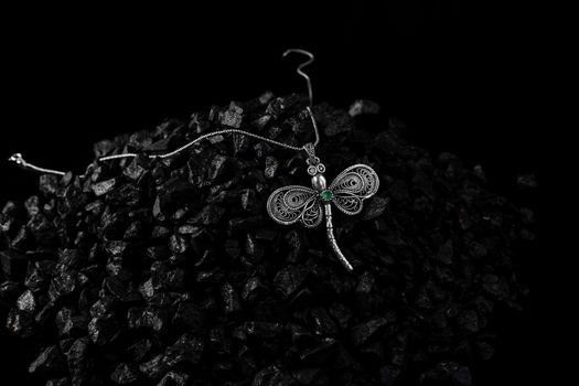 Unique handmade white gold dragonfly pendant with an emerald on a bunch of small black stones. Creative photo of unique jewellery.
