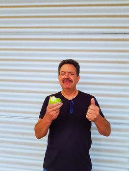 Portrait of a man in front of light background is eating a green sour apple and grimacing.