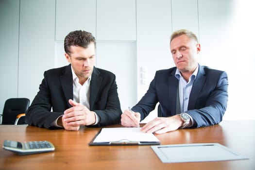 Two business people signing a document at conference table