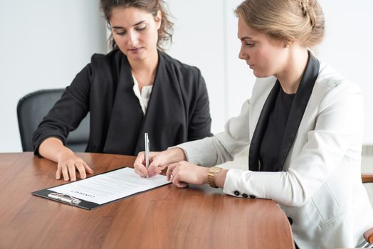 Two business women signing a document at conference table