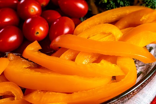 Slices of orange bell peppers and whole grape tomatoes are seen in a partial view of a tray of vegetables. The veggie snacks are in a glass platter.