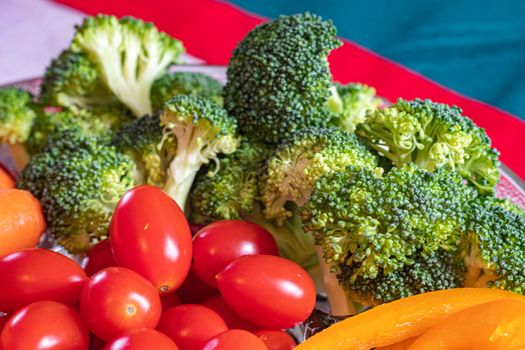 Cut broccoli florets and whole grape tomatoes are seen up close in a serving tray full of vegetables. Baby carrots and slices of orange bell peppers are just visible at the edges of the frame.