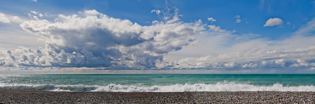 Sunny day, sky in clouds, blue sea with waves, pebble beach