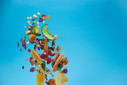 Dried and candied fruits and nuts flying on blue background. Stock photo of healty and nutrient food. Conceptual photo of vegan and vegetarian healty food.