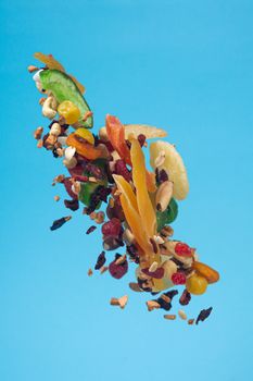 Dried and candied fruits and nuts flying on blue background. Stock photo of healty and nutrient food. Conceptual photo of vegan and vegetarian healty food.