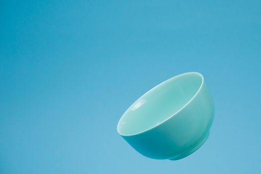 A blue ceramic mattle deep bowl for breakfast flying on blue background. Ideal photo for levitation of food and fruits or nuts.