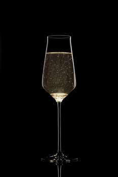 An unusual thin filled champagne glass with bubbles isolated on black background. Stock photo of luxury life. Conceptual photo of refined champagne. 