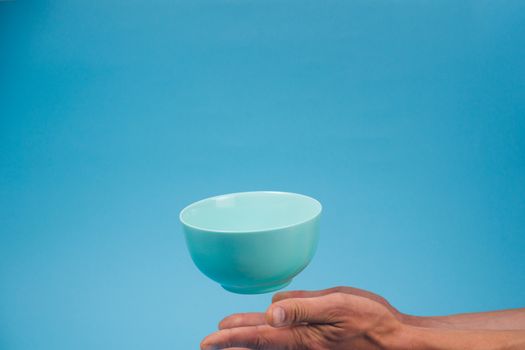 A blue ceramic mattle deep bowl for breakfast flying under male hands on blue background. Ideal photo for levitation of food and fruits or nuts.