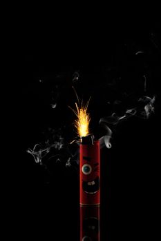 A stock photo of a red sparkling lighter with sparkles and white smoke isolated on black background.