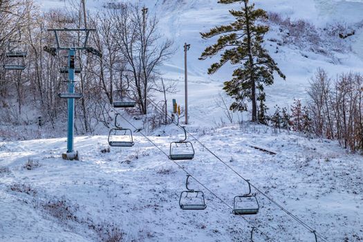A chairlift is seen on the side of a ski hill, its seats hanging empty and motionless as the hill is prepared for skiers and snowboarders ready to hit the slopes.