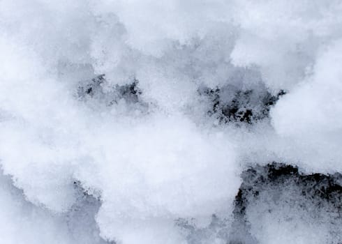 Clumps of snow on the side of a rock are viewed up close showing some of their texture and detail.