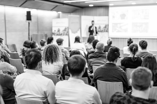 Speaker giving talk at business event. Audience at the conference hall. Business and Entrepreneurship concept. Focus on unrecognizable people in audience. Black and white.