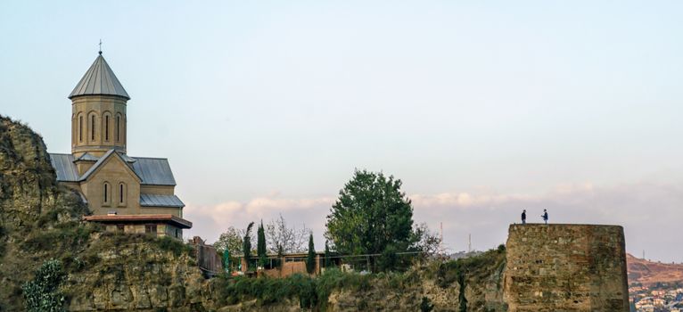Christian church on the mountain and old antique fortress on the background of the city landscape in Georgia