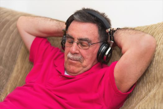 Senior man in headphones fall asleep in the sofa listening to music