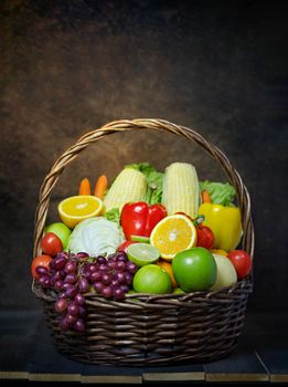 fresh vegetables and fruits in wicker basket over wooden background