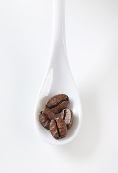 Overhead view of roasted coffee beans on white porcelain spoon