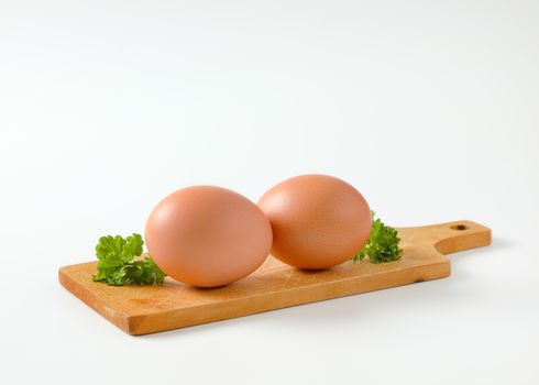 Two brown eggs on wooden cutting board