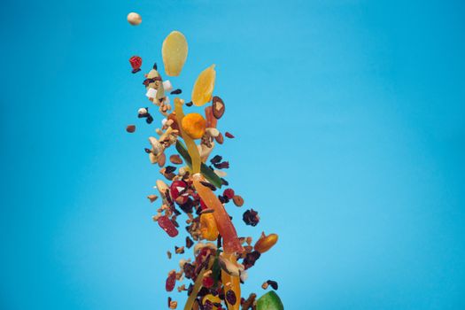 Dried and candied fruits and nuts flying on blue background. Stock photo of healty and nutrient food. Conceptual photo of vegan and vegetarian healty food.