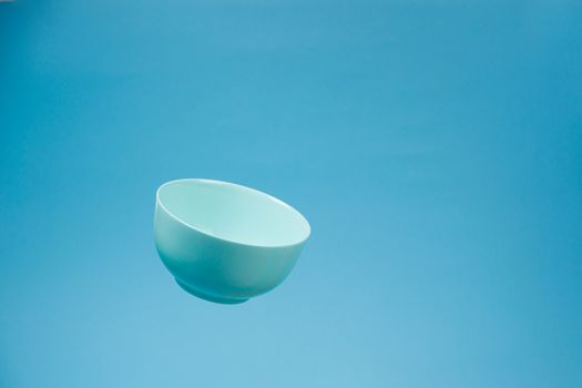 A blue ceramic mattle deep bowl for breakfast flying on blue background. Ideal photo for levitation of food and fruits or nuts.