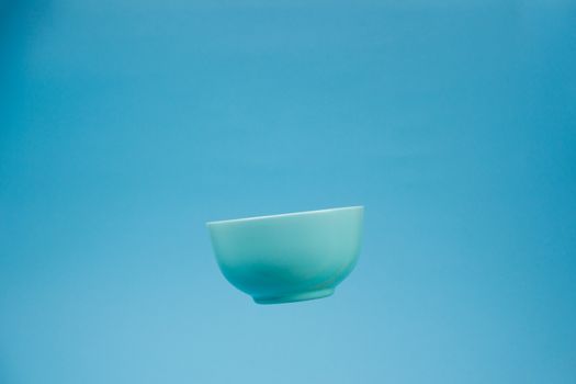 A blue ceramic mattle deep bowl for breakfast flying on blue background. Ideal photo for levitation of food and fruits or nuts.