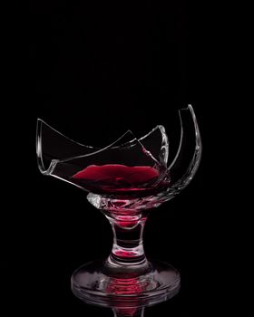 An unusual photo of cracked wine glass with few wine inside isolated on black background. Conceptual photo of original image presentation of wine glass for drinking.